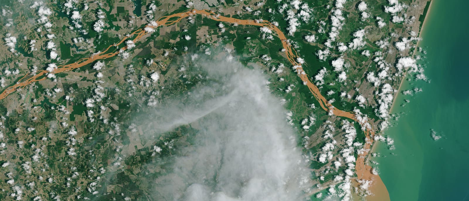 A satellite view of the mouth of the Rio Doce, the river running orange with mine tailings and staining the Atlantic brown where it meets the sea.